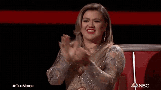 a woman is sitting in a chair and making a heart with her hands on a stage .