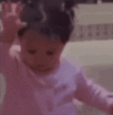 a baby girl in a pink shirt is standing in front of a glass door .