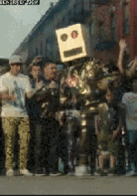 a group of people are standing around a robot with a box on its head .