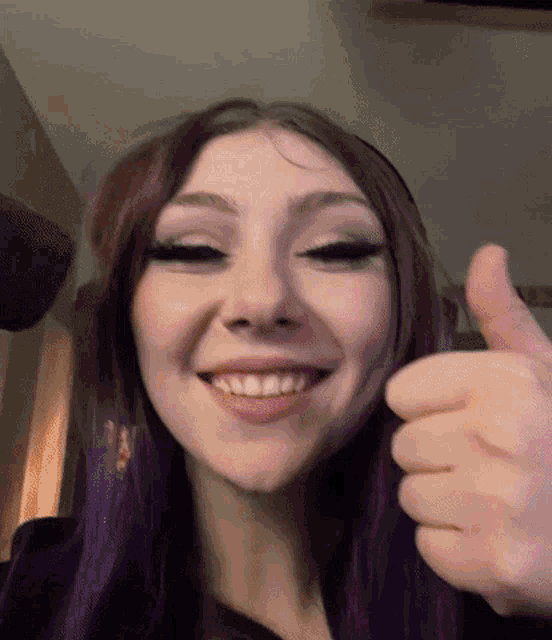 a young woman with purple hair is smiling and giving a thumbs up
