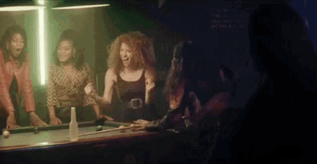 a group of women are sitting around a pool table .