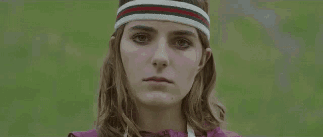 a woman wearing a headband and a sweater is looking at the camera .