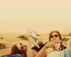 a man and a woman laying on a beach reading a magazine