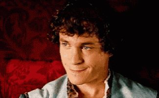 a man with curly hair and blue eyes is smiling while sitting on a red couch .
