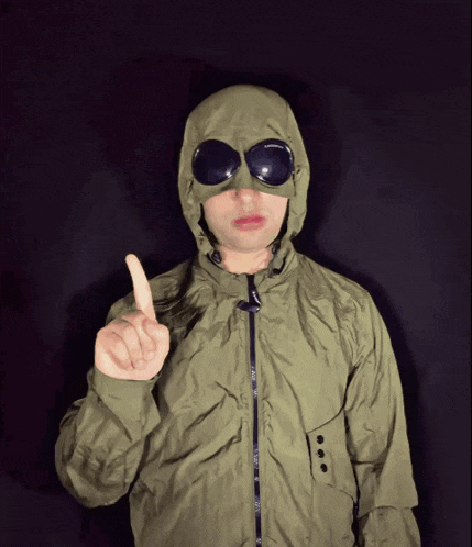 a man wearing a hooded jacket and goggles is pointing upwards