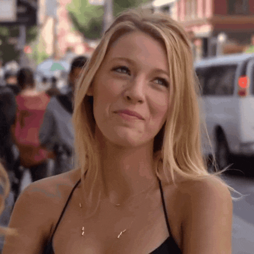 a woman wearing a black top and a gold necklace smiles