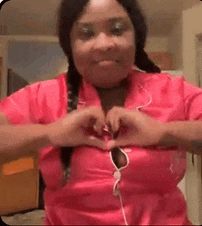 a woman in a pink shirt is making a heart with her hands over her chest .