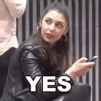 a woman in a leather jacket is holding a cell phone and making a funny face .
