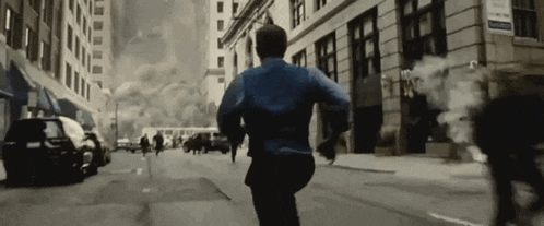 a man in a blue shirt is running down a city street .