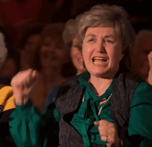 an elderly woman in a green shirt is screaming in a crowd .