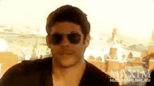 a man wearing sunglasses and a black shirt is standing in front of a building .