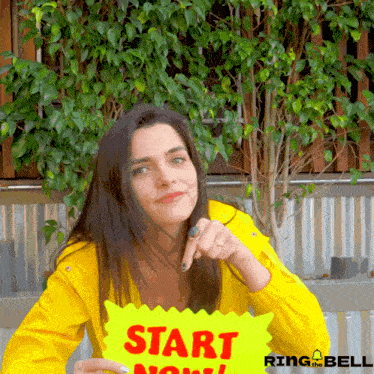 a woman in a yellow shirt is holding a yellow sign that says start now