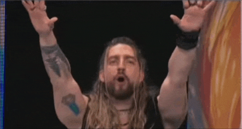 a man with long hair and a tattoo on his arm holds his arms up in the air