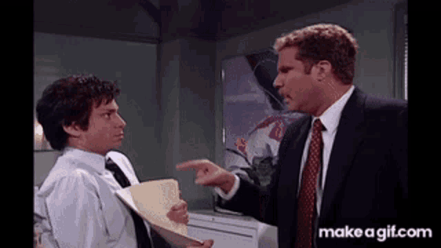 a man in a suit and tie is pointing at another man who is holding a folder .