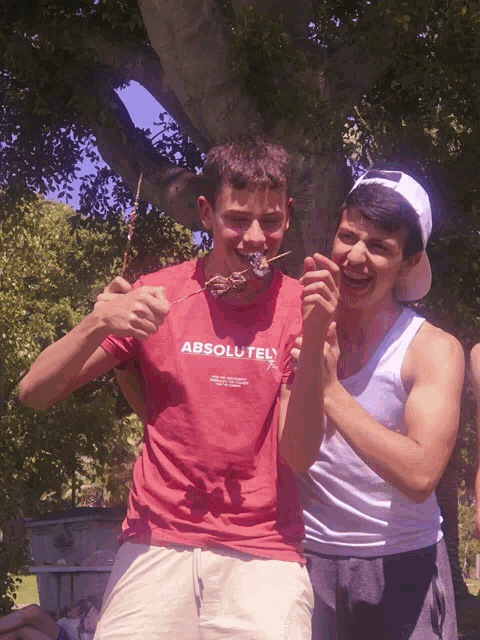a man wearing a red shirt that says " absolute " holds a stick in his mouth