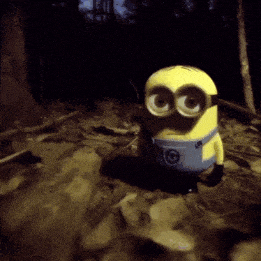 a toy minion is standing on a pile of leaves in the woods
