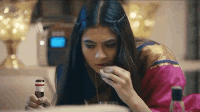 a woman is sitting at a table with a bottle of alcohol in her hand and eating food .