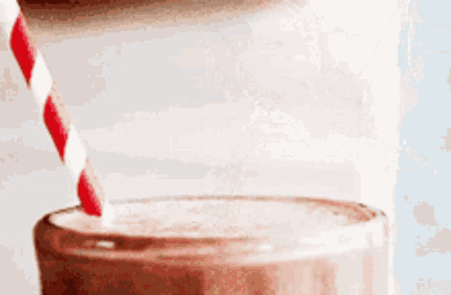 a milkshake with a red and white striped straw being poured into it