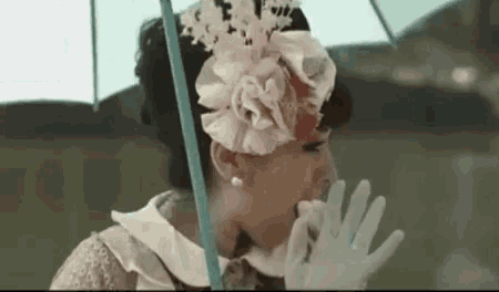 a woman wearing a hat and gloves is holding an umbrella and eating something .