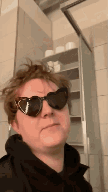 a man wearing heart shaped sunglasses in front of a shelf of toilet paper