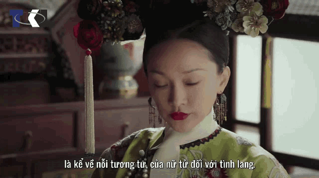 a woman in a green dress with red lipstick and flowers in her hair is talking in a video