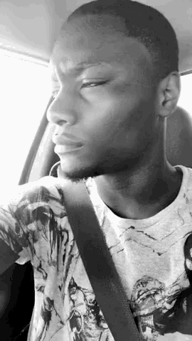 a black and white photo of a man sitting in a car with his eyes closed and wearing a seat belt .