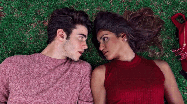 a man and a woman are laying in the grass and looking at each other