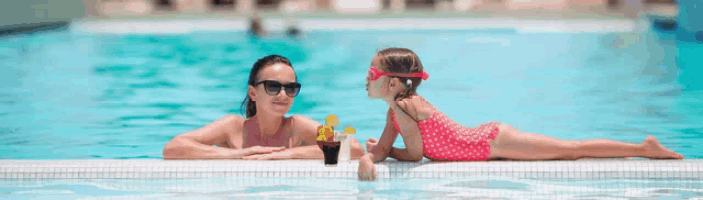 a woman and a little girl are sitting on the edge of a swimming pool with drinks in their hands .