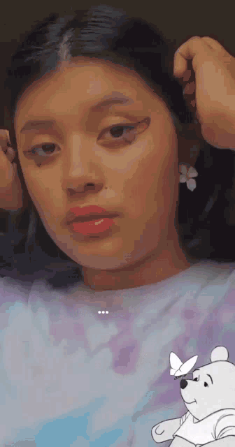 a woman is wearing a purple shirt and earrings with a winnie the pooh drawing on her face .