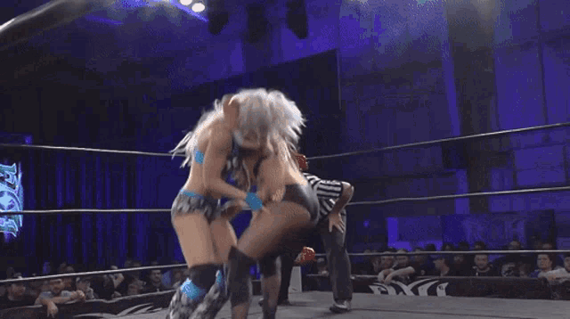 two women are wrestling in a ring while a referee looks on