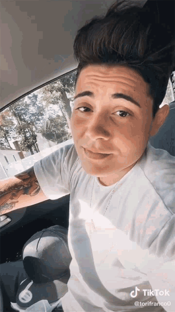 a man in a white shirt is sitting in the back seat of a car with a tiktok watermark