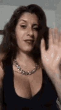 the woman is wearing a black tank top and a necklace and waving her hand .