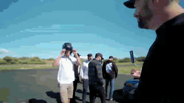 a group of men are standing on a road and one man is wearing a helmet