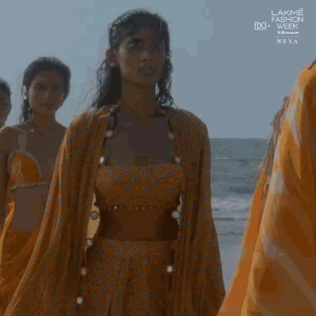 a group of women walking on a beach with a sign that says lakme fashion week next