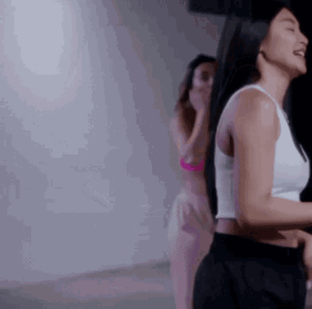 a woman in a white tank top and black shorts is standing next to a woman in a pink bra .