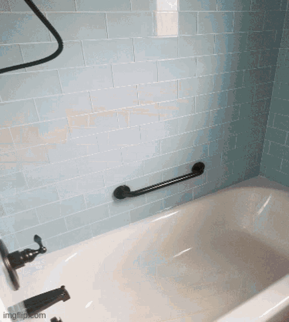 a bathtub in a bathroom with blue tiles and a black railing