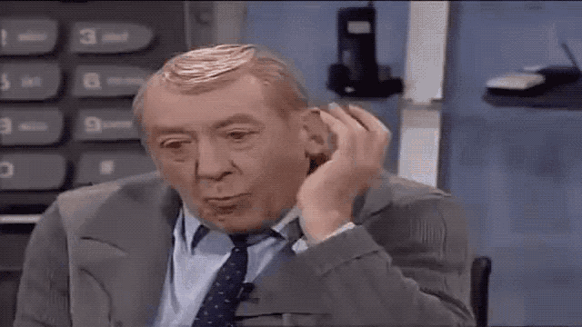 a man in a suit and tie is holding his hand to his ear while sitting in front of a calculator .
