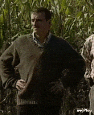 a man in a sweater is standing with his hands on his hips in a field .
