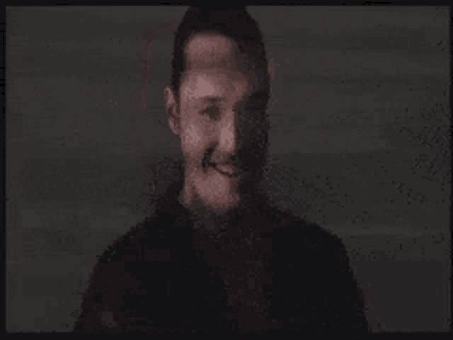 a man with a beard is smiling in a dark room in a blurry photo .