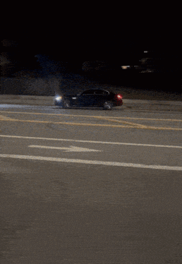 a black car is driving down a street with an arrow pointing to the right
