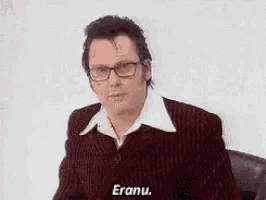 a man wearing glasses and a red suit is sitting in a chair and talking .