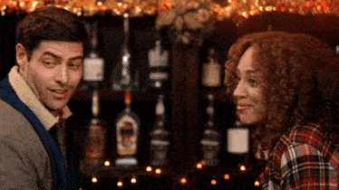 a man and woman are looking at each other in front of bottles of alcohol
