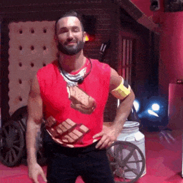 a man wearing a red shirt with a cookie on it is standing with his hands on his hips in a room .