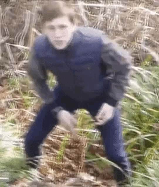 a man in a blue jacket and blue jeans is standing in the grass .