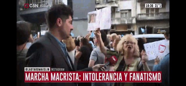 a man stands in front of a crowd of people holding signs and a c5n logo on the bottom