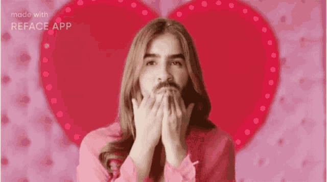 a man with a beard and long hair is blowing a kiss in front of a pink heart .