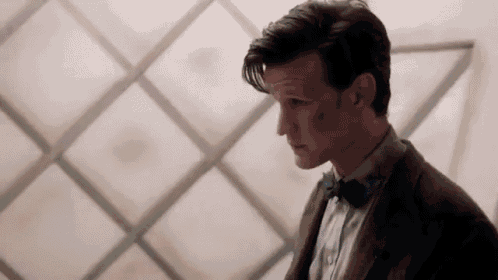 a man in a suit and bow tie is standing in front of a wall with squares on it .