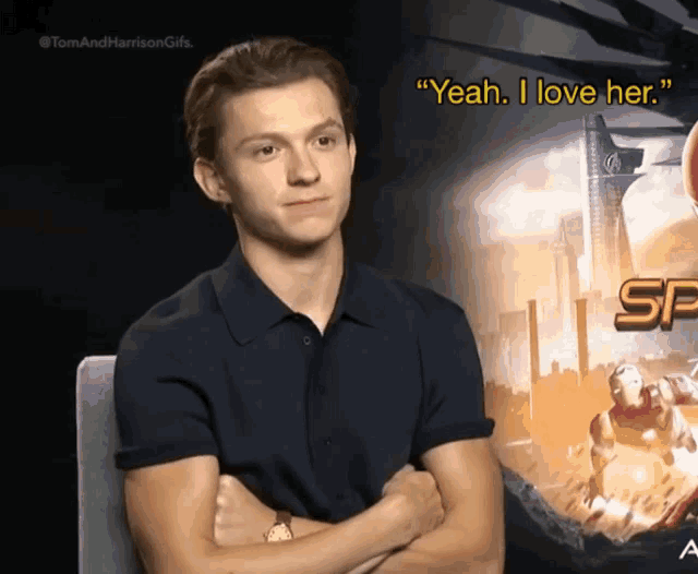 a man in a black shirt is sitting with his arms crossed in front of a sign that says yeah i love her