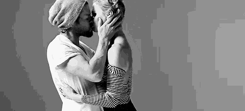 a man and a woman are kissing in a black and white photo . the woman is wearing a striped shirt .