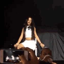a woman is sitting on a chair on a stage while a man takes a picture with a cell phone .
